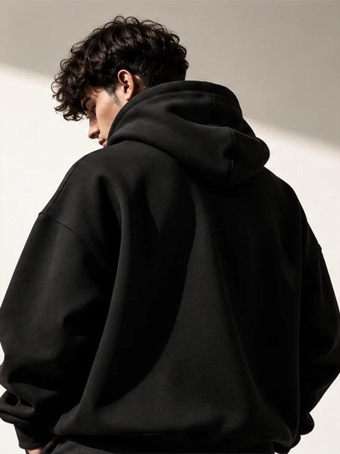 Model seen from behind wearing a black hoodie, photographed in a studio