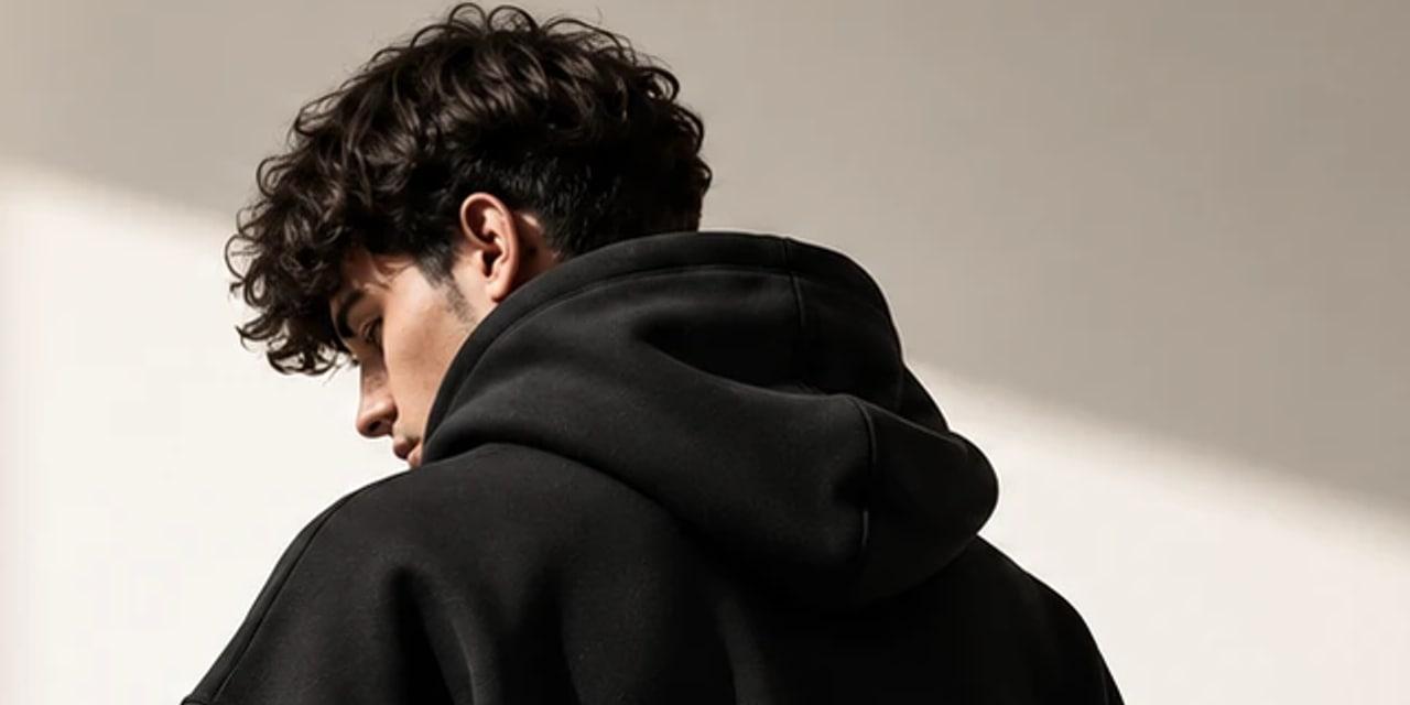 Model in profile, the hood of the black hoodie resting on the shoulders